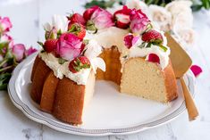 a white plate topped with a cake covered in frosting and strawberries next to flowers