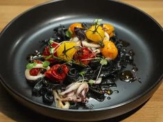 a black plate topped with lots of food on top of a wooden table