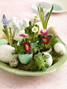 an arrangement of flowers and eggs in a green bowl on a pink tablecloth with other decorations