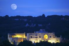 the moon is setting over an old building with lights on and trees in front of it