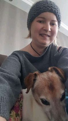 a woman sitting on a couch with a dog in her lap and smiling at the camera