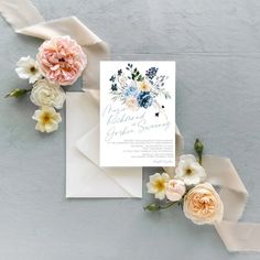 the wedding stationery is laid out on top of an envelope with flowers and ribbon