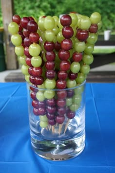 grapes are arranged in the middle of a glass vase on top of a blue table cloth