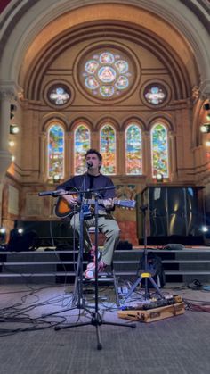 a man playing guitar in front of a stained glass window at a church with other instruments