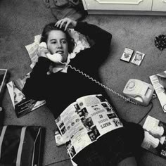 a woman sitting on the floor talking on a cell phone and holding a magazine in her hand