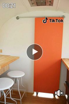 an orange door is in the corner of a room with three stools and a table