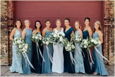 a group of women standing next to each other in front of a brick wall holding bouquets