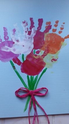 handprinted flowers are tied to a blue wall with pink ribbon on the bottom