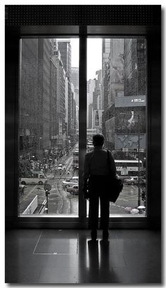 a man standing in front of a window looking out at a city street filled with traffic