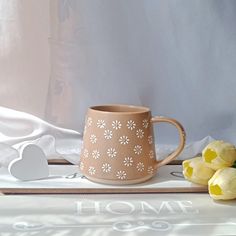 a coffee cup sitting on top of a table next to yellow tulips and paper hearts