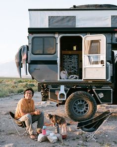 a man sitting in front of a camper with his dog on the ground next to him