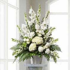 a vase filled with white flowers sitting on top of a table next to a window