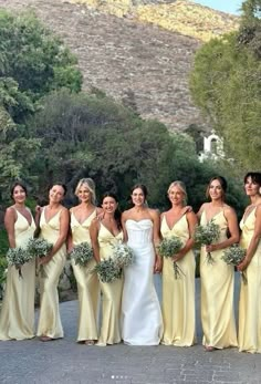 a group of women standing next to each other in front of trees and bushes on a road