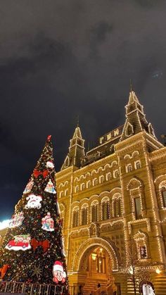 a christmas tree in front of a large building with lights on it's sides