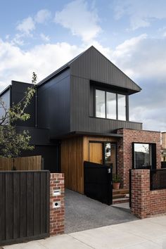 a modern house with black siding and wood accents on the front door, along with brick walls