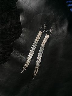 two pairs of silver earrings with long fringes on black leather background, close up