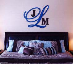 a bed with blue and purple pillows in front of a large metal j on the wall