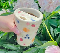 a hand holding a cup with flowers in the background