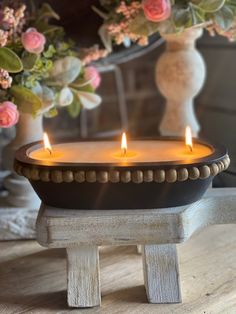 two lit candles sitting on top of a wooden table next to flowers and vases