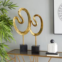 two golden metal sculptures sitting on top of a table next to a potted plant