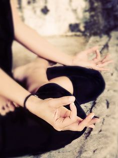 a woman sitting on the ground with her hands up to her chest and holding something in one hand