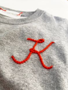 an embroidered t - shirt with the letter k on it's chest and red thread