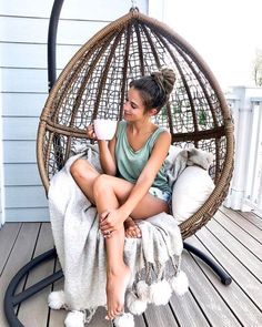 a woman sitting in a hanging chair with a cup