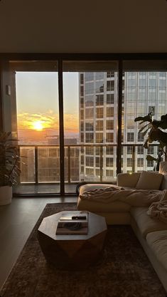 a living room filled with furniture and a large window overlooking the city at sunset or dawn