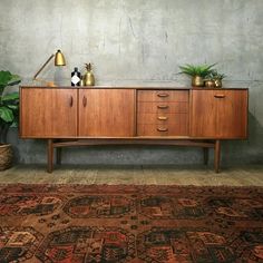 a wooden sideboard sitting on top of a rug next to a potted plant