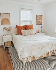 a white bed sitting in a bedroom next to a window with lots of pillows on top of it