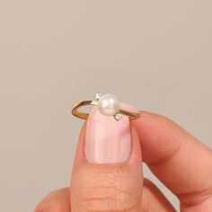 a woman's hand holding a ring with a pearl and diamond on the middle