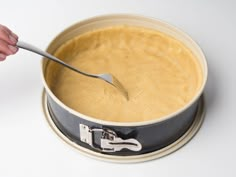 a person holding a spoon in a bowl filled with batter on top of a white table