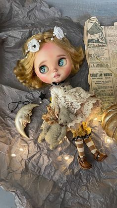 a doll with blue eyes and blonde hair laying on crumpled paper next to a teddy bear