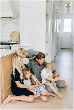 a family is sitting on the floor in their kitchen and posing for a photo together