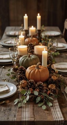 a wooden table topped with lots of candles and plates covered in pineconi, pumpkins and greenery