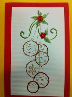 a christmas card with baubles and holly on the top, hanging from a red frame