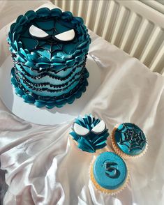 a blue cake and cupcakes on a white tablecloth with silver foiling