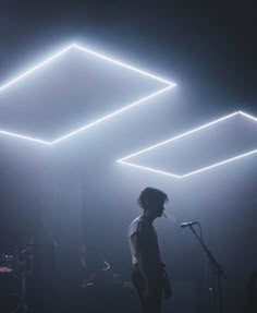 a man standing in front of a microphone on stage with lights shining down from the ceiling