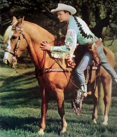 a man sitting on the back of a brown horse in a grassy field next to trees