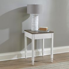 a white table with a book and lamp on it next to a gray painted wall