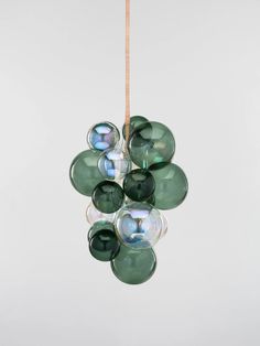 a bunch of green glass balls hanging from a string in front of a white wall