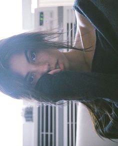 a woman with long hair and blue eyes posing for a photo in front of a radiator