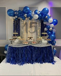 a table topped with blue and white balloons next to a number 15 cake on top of a table