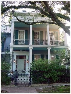 a large white house with green shutters and balconies on the front porch