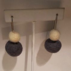 two wool balls are hanging from hooks on a white wall, one is gray and the other is yellow