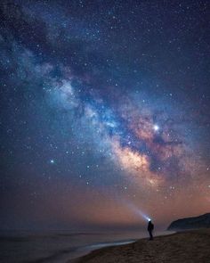 a man standing on top of a sandy beach under a night sky filled with stars