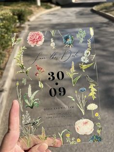 a person holding up a wedding card with flowers on the front and back, that says save the date