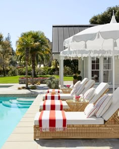 an outdoor pool with lounge chairs and umbrellas next to the swimming pool, surrounded by palm trees