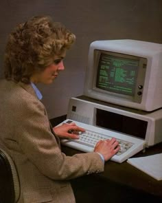 a woman sitting in front of a computer with a keyboard and monitor on top of it