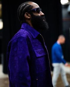 a man with a long beard and sunglasses standing in front of a black background wearing a purple shirt